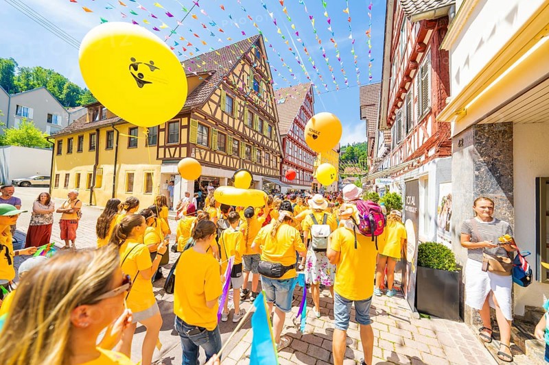 People in yellow T-shirts celebrate in a narrow street with half-timbered houses under colourful garlands, 950 years Calw, parade Calw, Black Forest, Germany