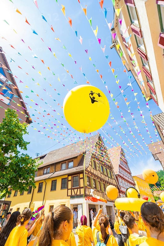 Yellow balloons rise into the sky above a busy street with historical flair and colourful pennants, 950 years of Calw, Calw parade, Black Forest, Germany