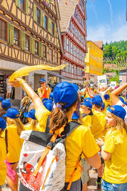 A group of children in yellow shirts and blue caps celebrates in an old town with half-timbered houses, 950 years of Calw, Calw parade, Black Forest, Germany