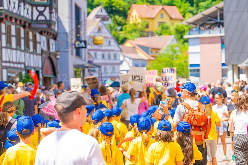 Children in yellow shirts and blue caps march with signs through a busy half-timbered street, 950 years of Calw, Calw parade, Black Forest, Germany
