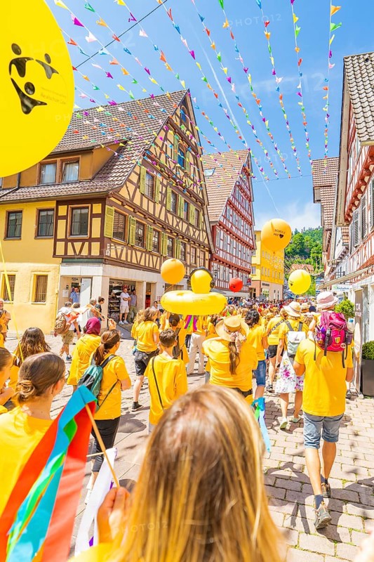 People in yellow clothes walk under colourful pennants in a narrow street in front of traditional houses, 950 years Calw, parade Calw, Black Forest, Germany