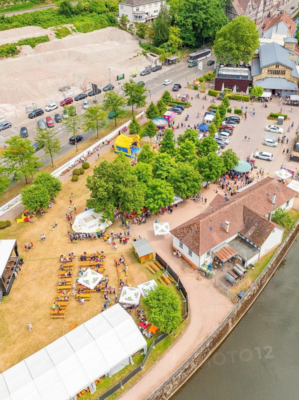 Aerial view of people at an event on a green area, surrounded by trees and river, 950 years Calw, Calw parade, Black Forest, Germany