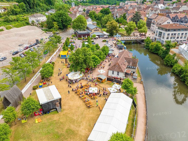 Aerial view of a town festival with people and tents on the riverbank next to historical architecture, 950 years of Calw, Calw parade, Black Forest, Germany