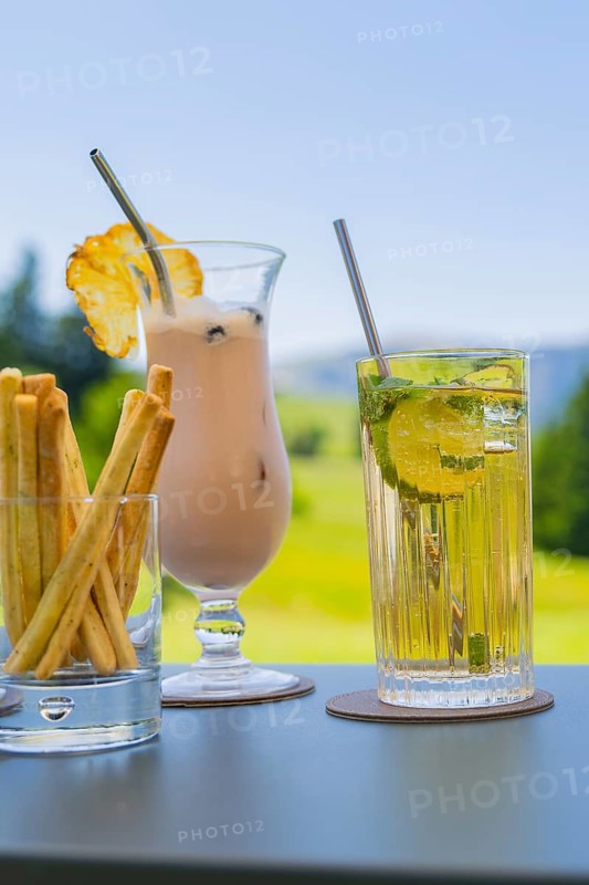 Two cocktails with decorative lemon and mint decorations in front of a summery landscape, Alpe di Siusi, Dolomites, South Tyrol, Italy