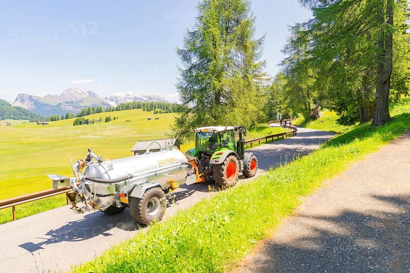 A tractor drives on a road in the middle of a green and sunny mountain landscape, Alpe di Siusi, Dolomites, South Tyrol, Italy