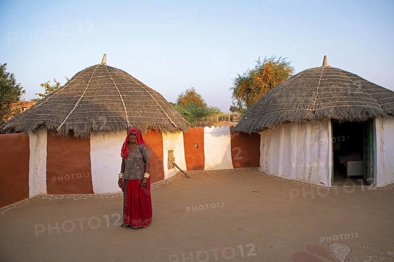 Indian woman, 55 years old, desert dweller, behind typical round buildings in the Thar Desert or Great Indian Desert, near Jaisalmer, Rajasthan, India