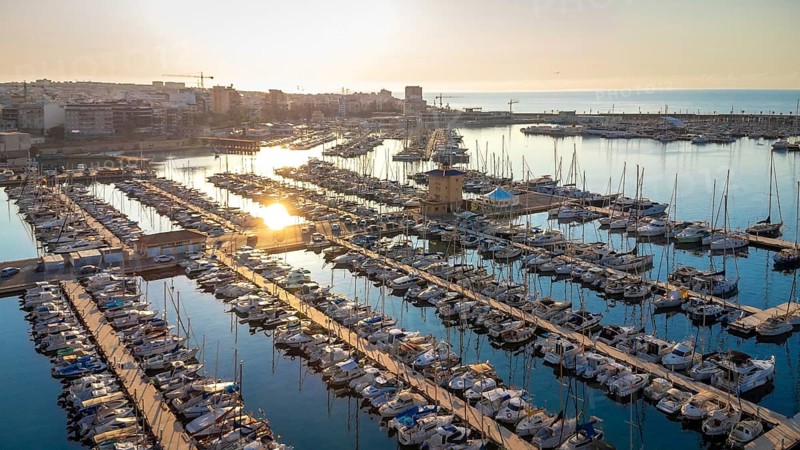 Golden sunrise reflecting on calm waters of torrevieja marina, showcasing docked boats and the cityscape in the background