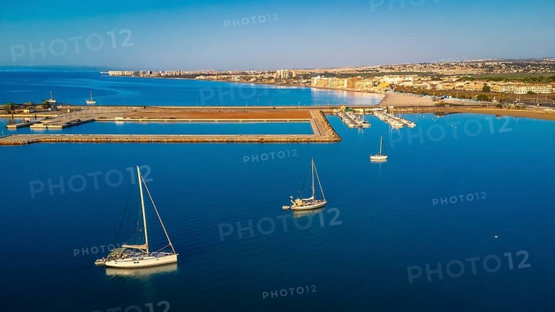 Stunning aerial view of sailboats floating on calm blue water near the coastline of torrevieja city, featuring a vibrant cityscape under a clear sky