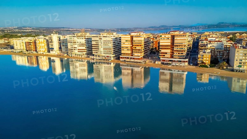 Aerial view of torrevieja skyline reflecting on calm mediterranean sea at sunrise, with colorful buildings and tranquil waters creating a peaceful scene