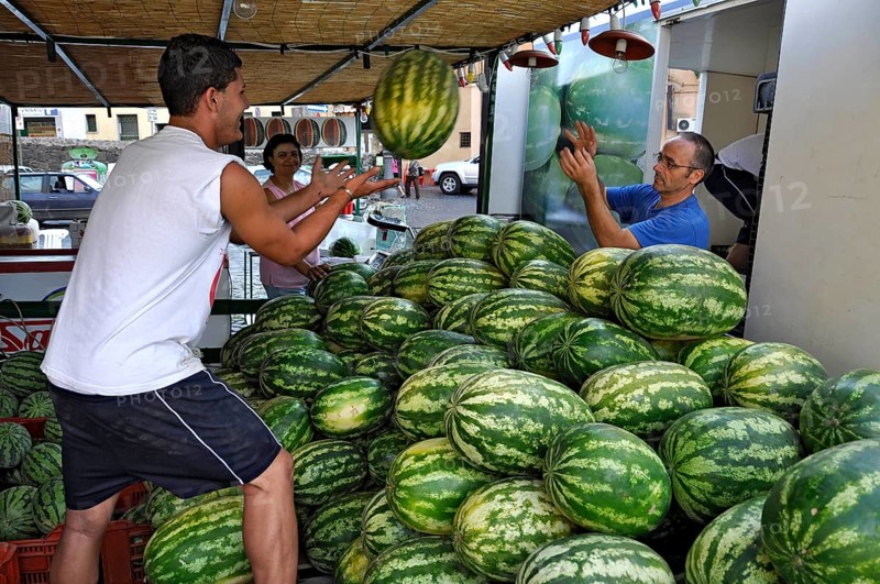 Farmers throwing watermelons (Citrullus lanatus) to each other, setting up a market stall, weekly market market, historic centre, Bracciano, metropolitan city of Rome, Lazio, Italy