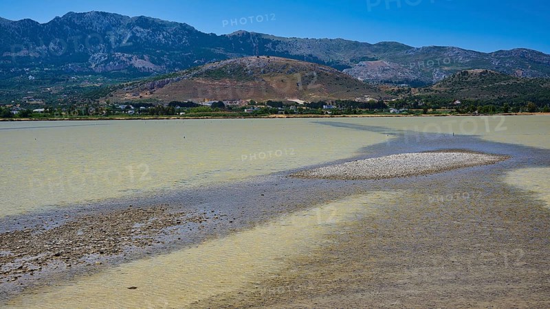 A lake with a long gravel bank and mountains in the background under a blue sky, salt lake, Tigaki, nature reserve, hydro biotope, Kos, Dodecanese, Greek Islands, Greece