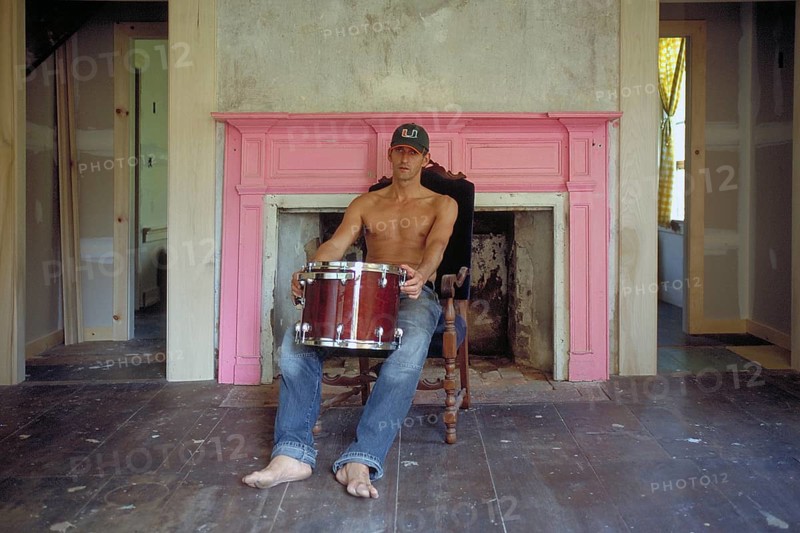 Young man with his drums in an empty room in front of a fireplace, New Jersey, USA