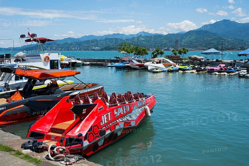 A red jet boat in the foreground of a harbor surrounded by other boats and mountains in the background, Batumi, Black Sea, Ajara region, Adjara, Autonomous Republic, Georgia