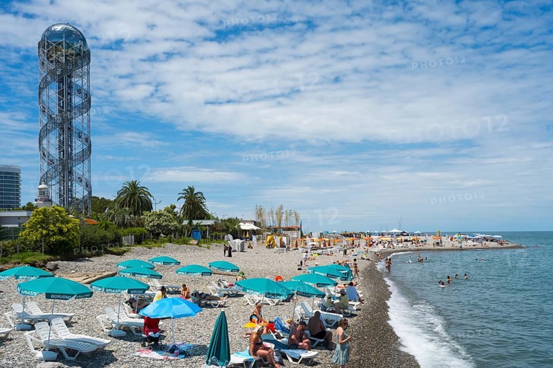 Beach with many visitors under umbrellas, a view of the sea and a distinctive tower in the background, Alphabetic Tower, Georgian Alphabet Tower, Miracle Park, Batumi, Black Sea, Ajara region, Adjara, Autonomous Republic, Georgia
