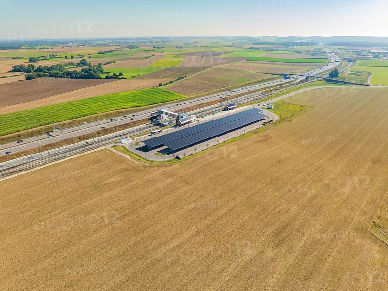 Solar system and motorway run parallel through wide fields under clear skies, e-charging park, Merklingen, Germany