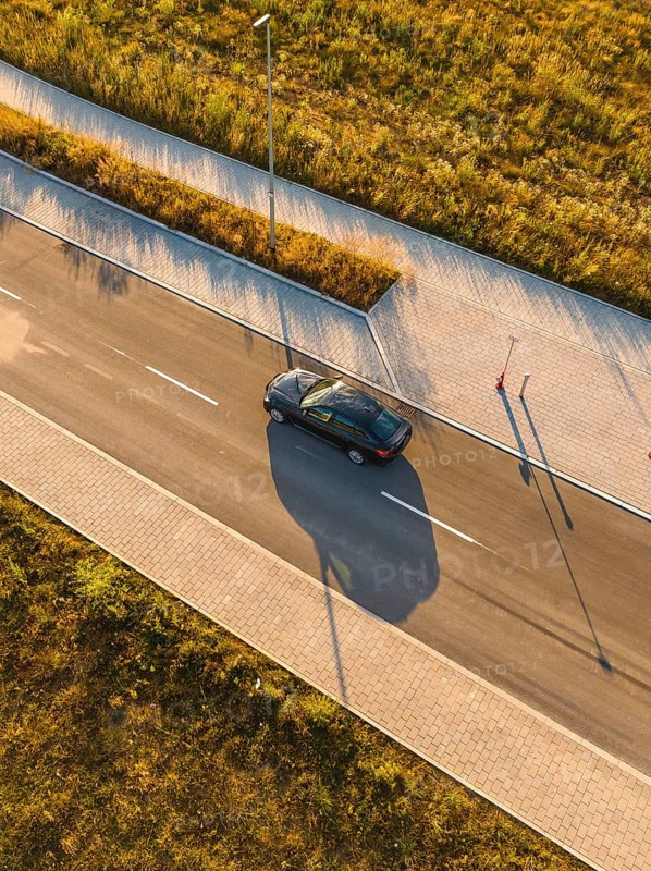 Aerial view of moving car and long shadows on paved road, BMW i7 electric car, deer e-car sharing, Calw, Germany