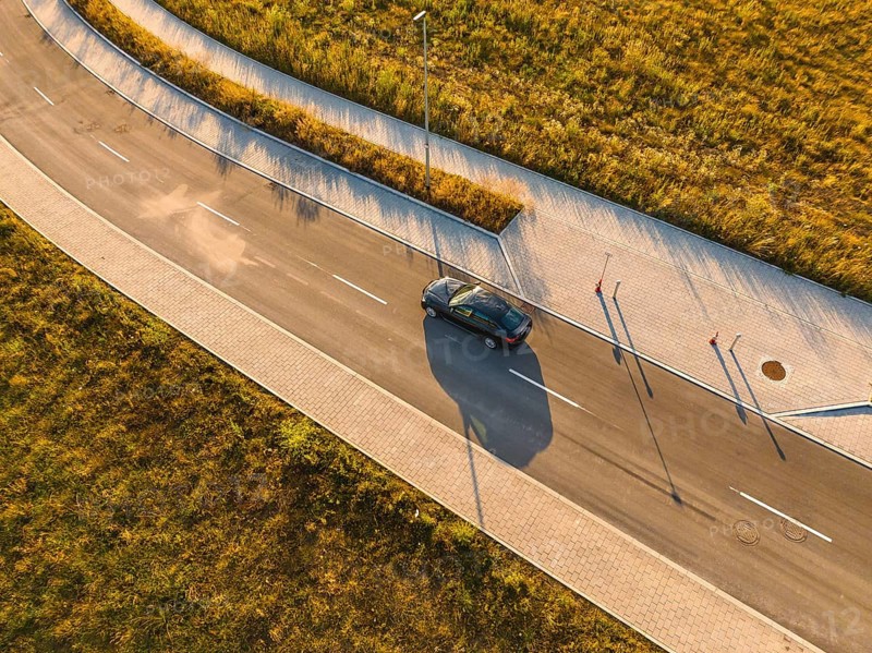 Aerial view of a car on a paved road next to a field in sunlight, BMW i7 electric car, Deer E-Carsharing, Calw, Germany
