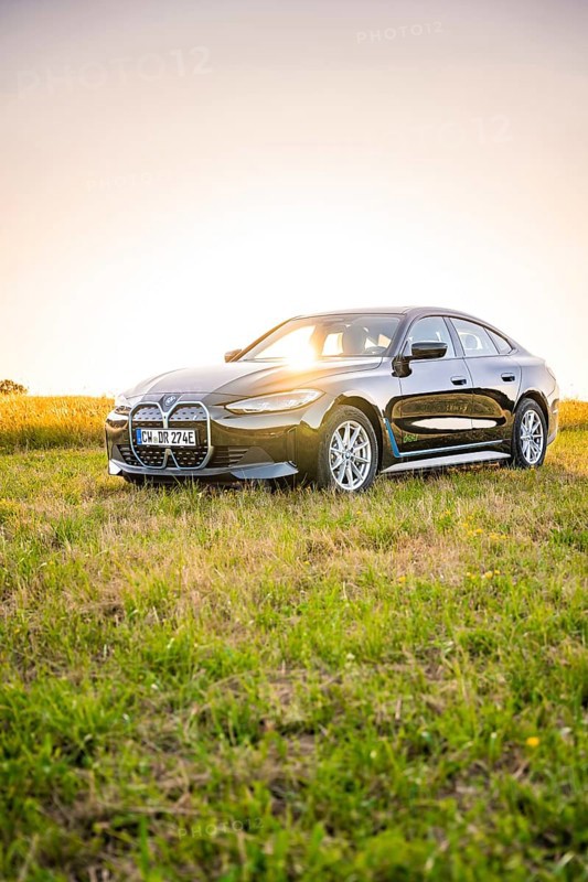 Black electric car in a meadow at sunset, the light falls on the car surrounded by green, BMW i7 electric car, Deer e-Carsharing, Calw, Germany