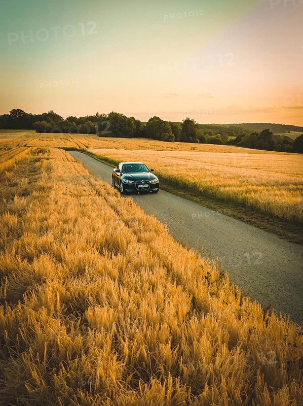 Vehicle moving on a country road through vast, golden cornfields in the evening light, BMW i7 electric car, Deer e-Carsharing, Calw, Germany