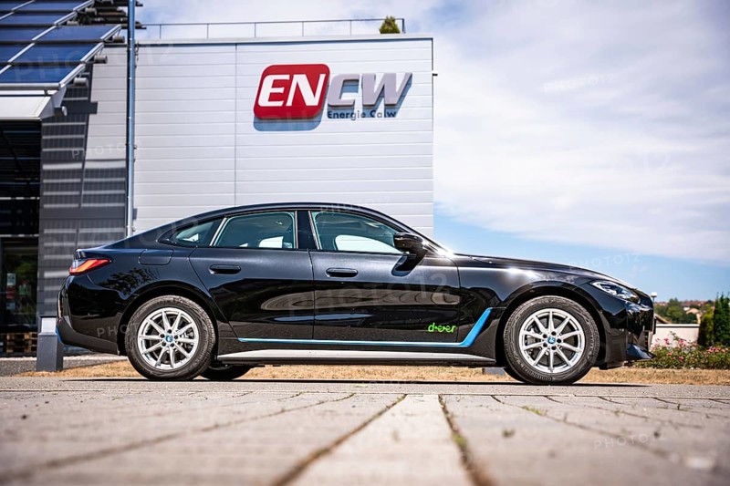 Black car in front of a building with a large company logo under blue sky, BMW i7 electric car, Deer e-Carsharing, Calw, Germany