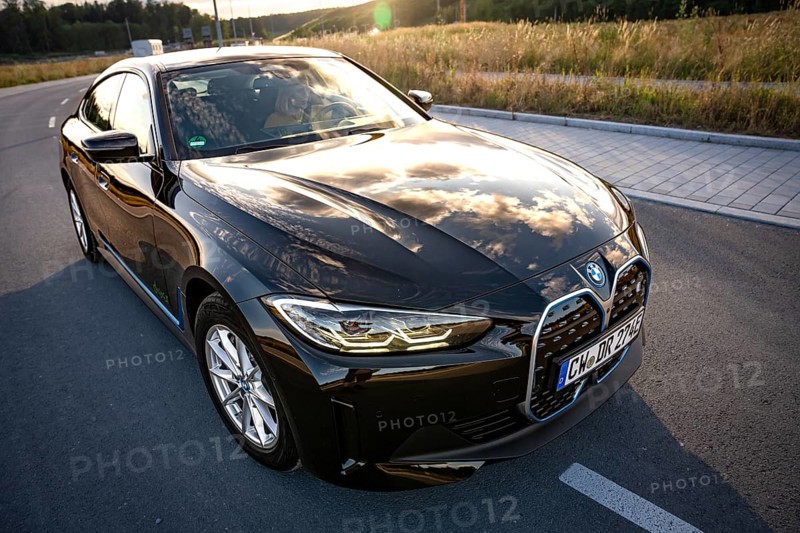 A black car on a road with reflecting sky and a field, BMW i7 electric car, Deer e-Carsharing, Calw, Germany