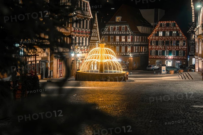 Idyllic night scene with illuminated fountain and traditional buildings in the city center, Calw, Black Forest, Germany