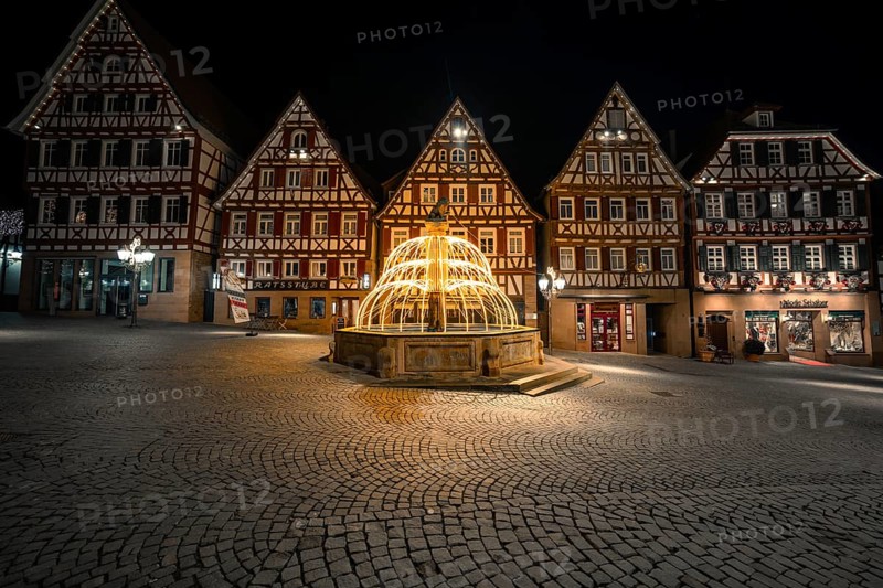 Illuminated fountain in a historic city center with half-timbered buildings at night, Calw, Black Forest, Germany