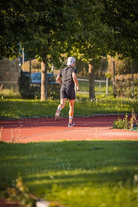A jogger runs on a red track in the countryside, surrounded by trees on a sunny day, triathlon, Calw, Germany