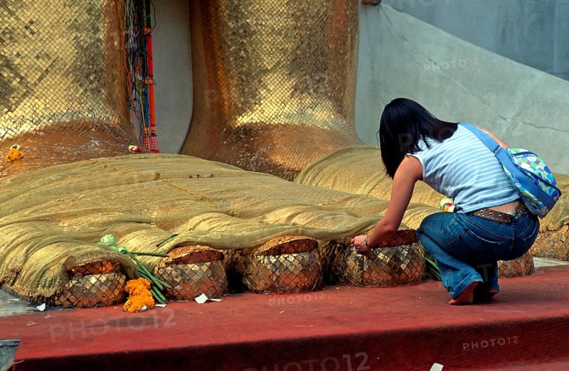 A young woman places flowers on the toes of the standing Buddha at Wat Indrawihan, Bangkok, Thailand, December 2002, vintage, retro, old, historic