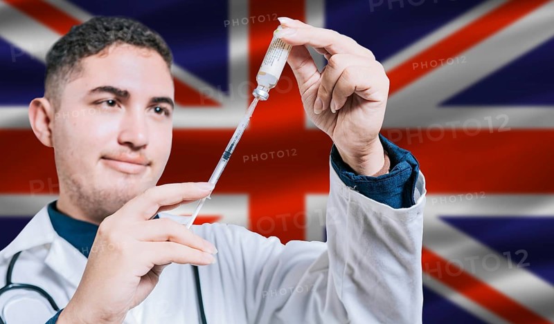 Doctor holding syringe on United Kingdom flag background. Medical professional holding syringe with British flag in the background