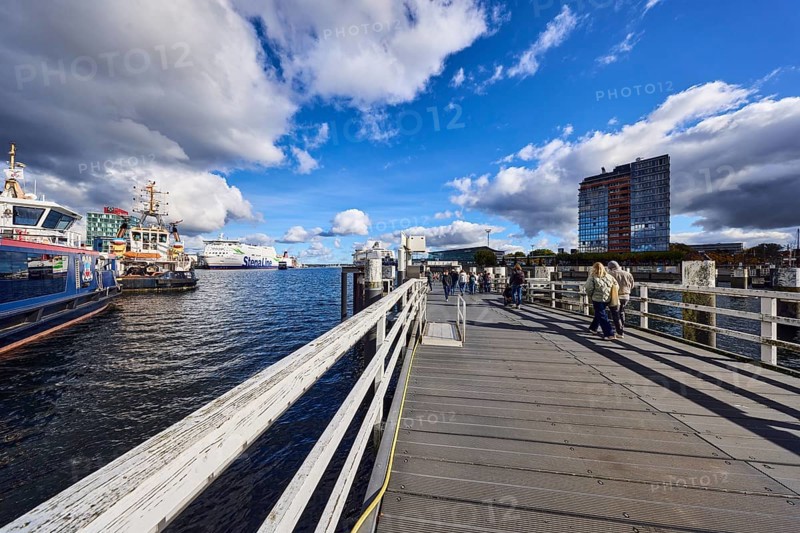 Kiel Fjord, station bridge, pier, wooden railings, wharf, ferries, harbor and sea tugs, ships, high-rise center at Germania port, pedestrians as accessories, blue sky, cumulus clouds, stratocumulus clouds, white and dark clouds, Kiel, state capital, district-free city, Schleswig-Holstein, Germany