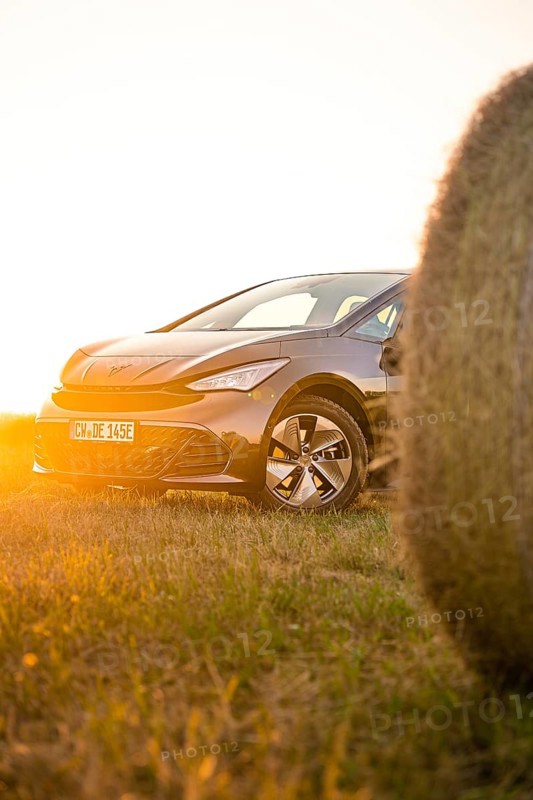 Car in the golden light of sunset in a meadow next to a hay bale, electric car Cupra, e-car sharing, Calw, Germany