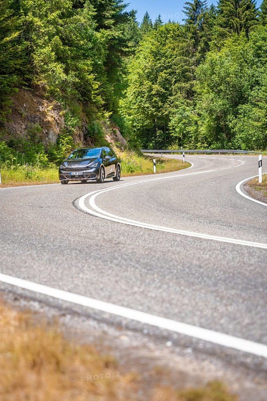Black car on winding country road along green forests in sunny ambiance, Cupra electric car, e-car sharing, Calw, Germany