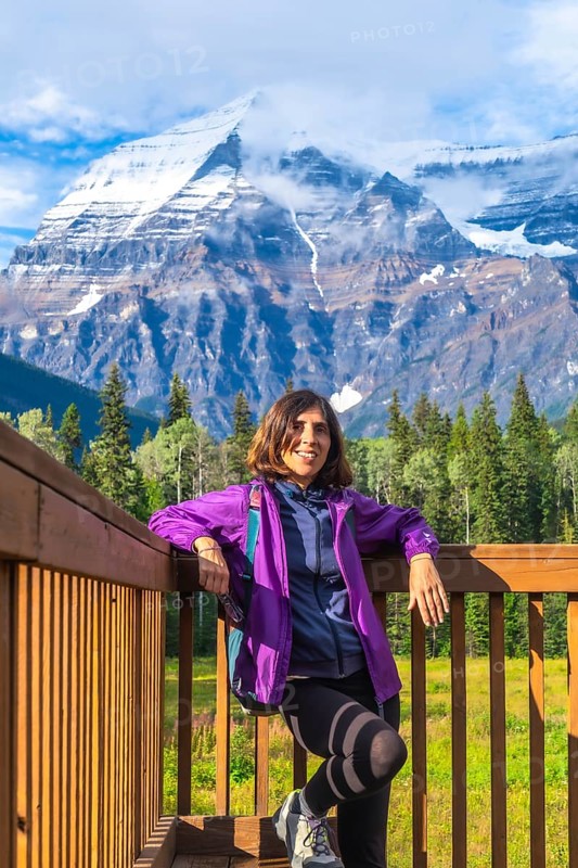 Female hiker is taking a break on a wooden platform, enjoying the breathtaking view of mount robson, the highest peak in the canadian rockies, british columbia, canada