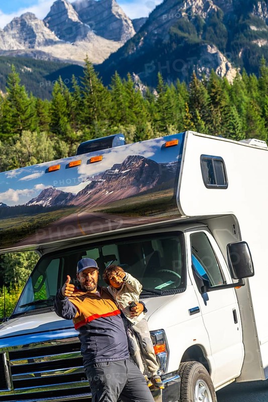 Father and son giving thumbs up in front of their rv, enjoying breathtaking views of mount robson in the canadian rockies during a memorable family road trip