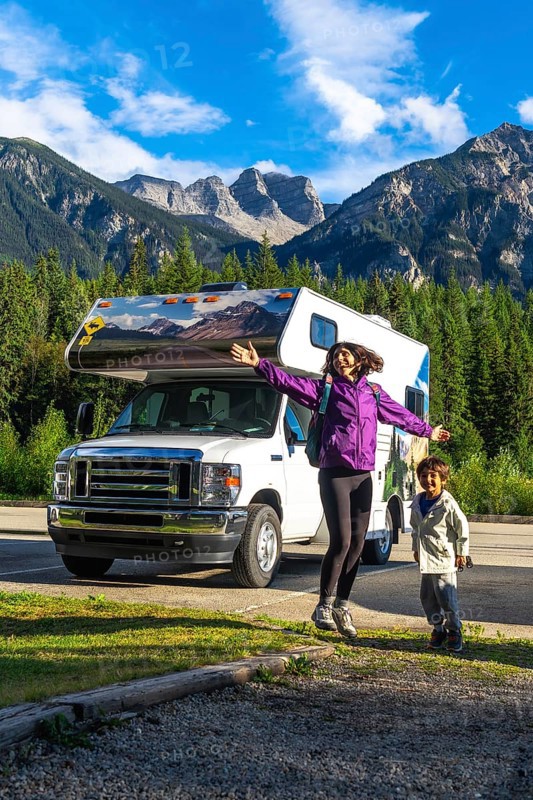 Happy mother and son are jumping in front of their recreational vehicle near mount robson in the canadian rockies, british columbia, canada, enjoying their summer vacation