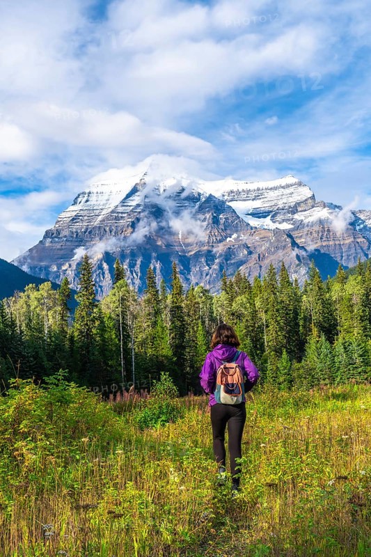 Female hiker walking through a meadow toward the majestic mount robson, the highest peak in the canadian rockies, enjoying the stunning beauty of british columbia
