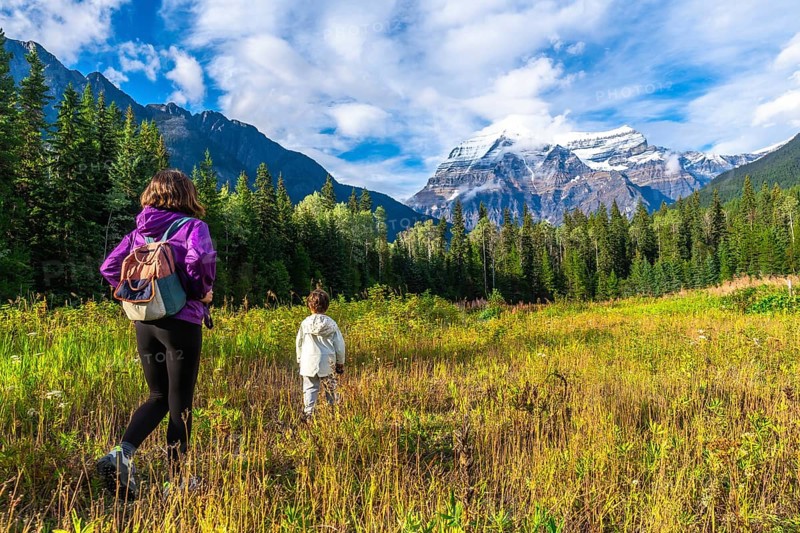 Hikers are enjoying a scenic walk through a meadow with majestic mount robson towering in the distance, showcasing the natural beauty of the canadian rockies in british columbia, canada