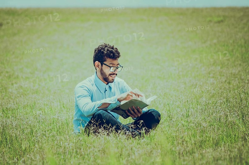 Young man on the grass reading a book, A person sitting on the grass reading a book, concept of people reading outside