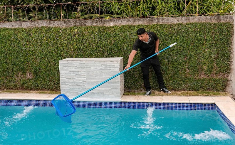 Swimming pool cleaning and maintenance concept. Maintenance person cleaning a swimming pool with skimmer, Worker cleaning a swimming pool with skimmer