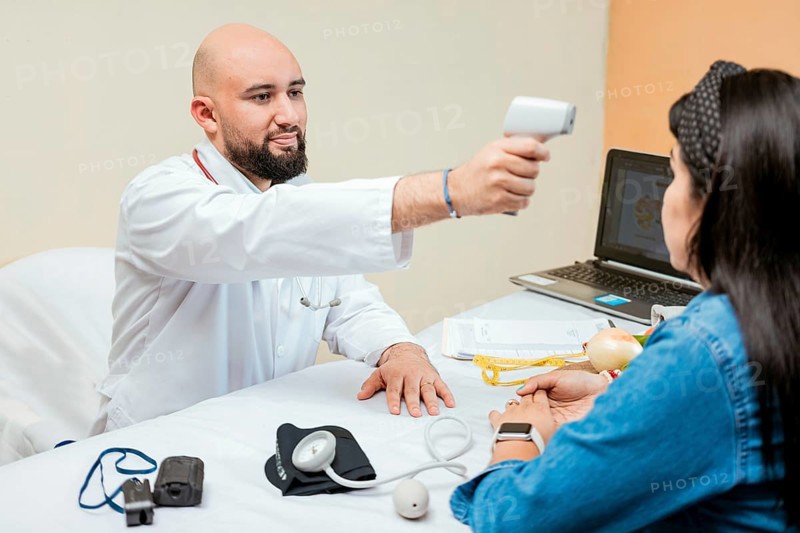 Doctor measuring temperature with infrared gun to female patient, Doctor taking temperature to woman patient in office, Male doctor taking temperature with gun to patient