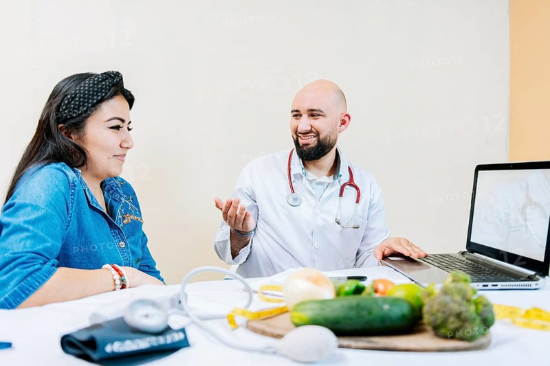 Smiling nutritionist explaining to a female patient, Nutritionist man talking to woman patient in office. Back view of a female patient talking to the nutritionist
