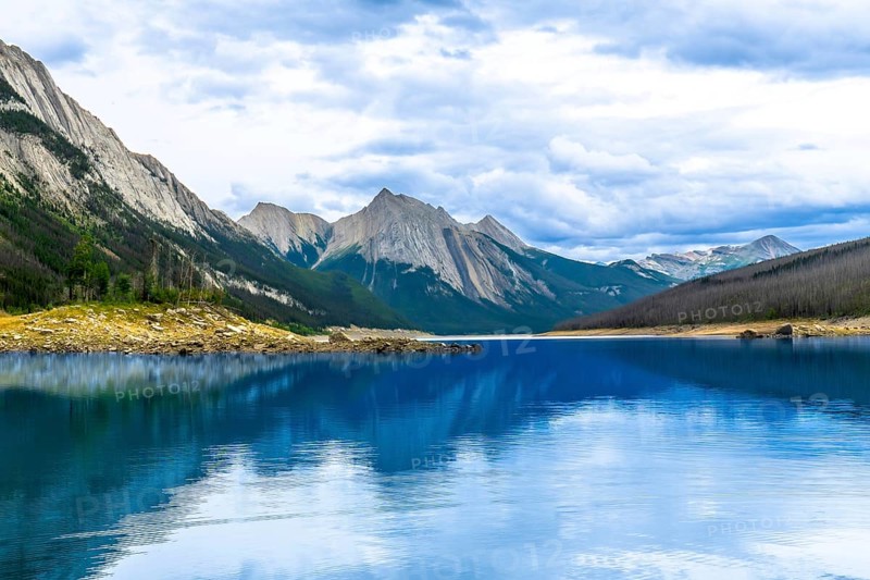 Calm turquoise water of medicine lake reflecting surrounding mountains under a cloudy sky in jasper national park, a unesco world heritage site, during a cloudy summer day