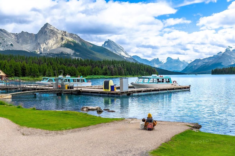 Tourists are enjoying the breathtaking view of maligne lake with tour boats and spirit island in the distance, surrounded by the majestic canadian rockies in jasper national park, alberta, canada