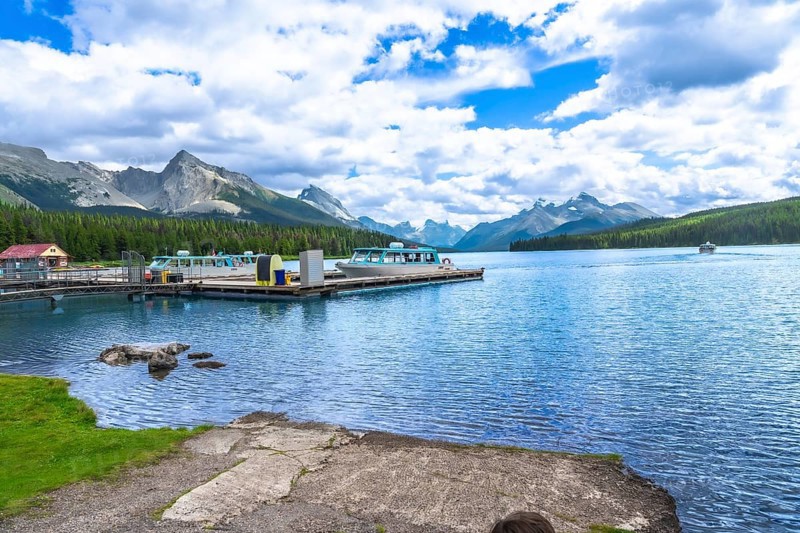 Tour boats are docked at maligne lake in jasper national park with a stunning view of the canadian rockies on a beautiful summer day with blue sky and clouds