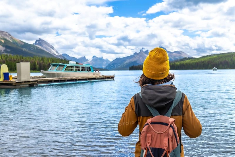Female tourist wearing a yellow beanie and carrying a backpack admires the stunning view of maligne lake and spirit island in jasper national park, alberta