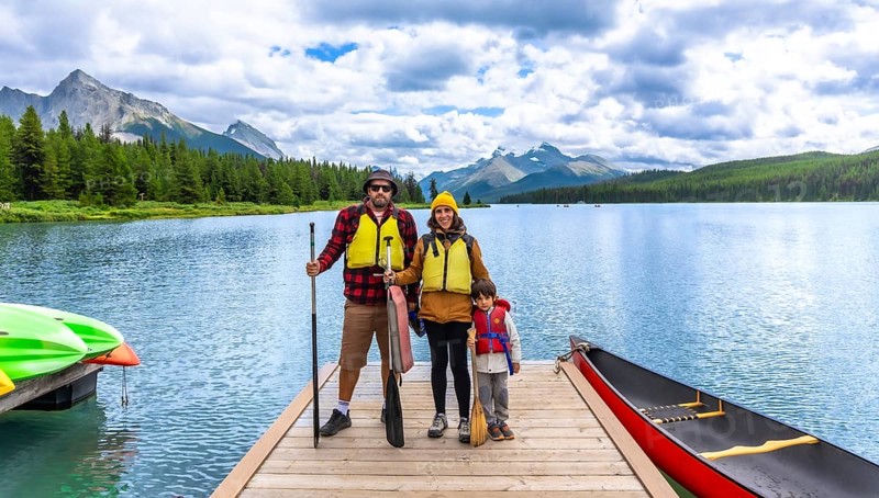 Family wearing life jackets and holding paddles, standing on a wooden dock with canoes and kayaks, enjoying a day of paddling on maligne lake in jasper national park