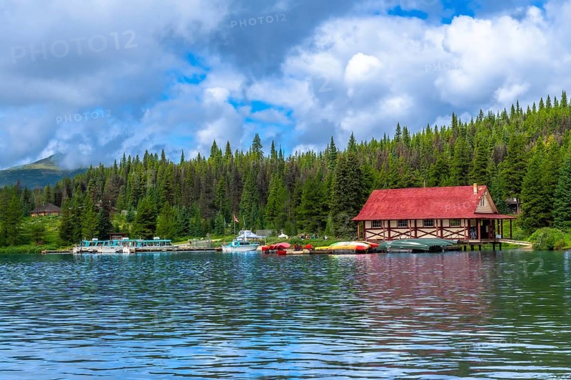 Colorful canoes and tour boats are docking at a boathouse with a red roof on maligne lake in jasper national park in the canadian rockies of alberta, canada, under a partly cloudy sky