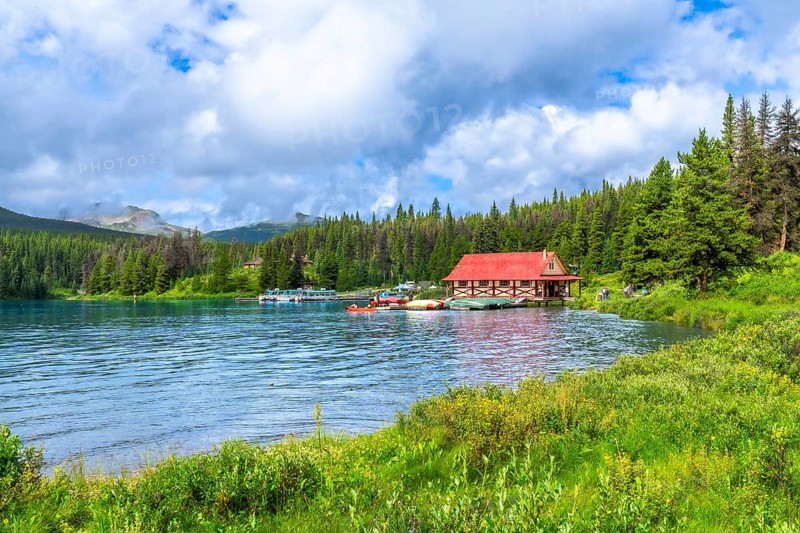 Beautiful summer landscape featuring a vibrant red roofed boathouse on the serene shores of maligne lake in jasper national park, alberta, with lush greenery and boats