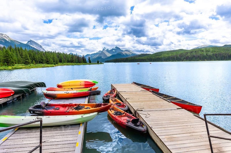Colorful canoes and kayaks resting on a wooden dock invite exploration of maligne lake's pristine waters, surrounded by the majestic canadian rockies under a cloudy sky